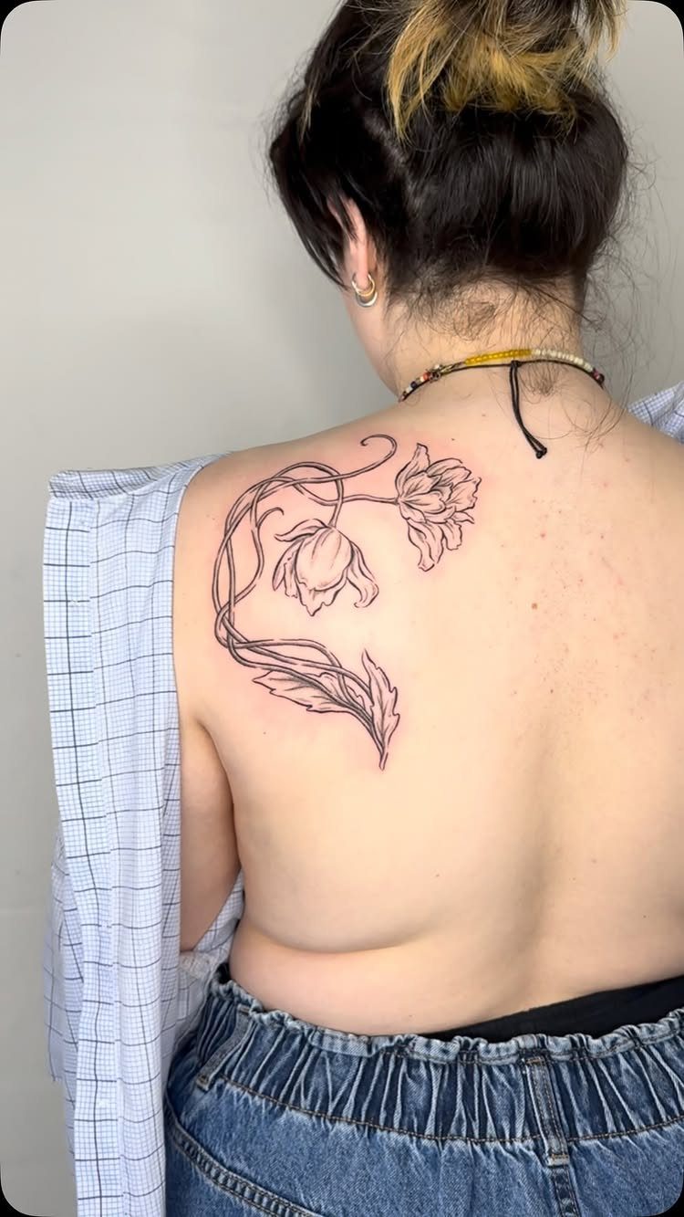Floral vine tattoo with two blooms on a person's left shoulder blade.
