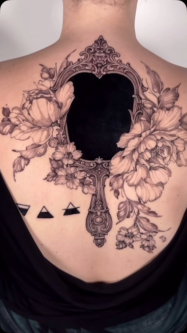 Ornate mirror frame tattoo surrounded by peonies on a person's upper back
