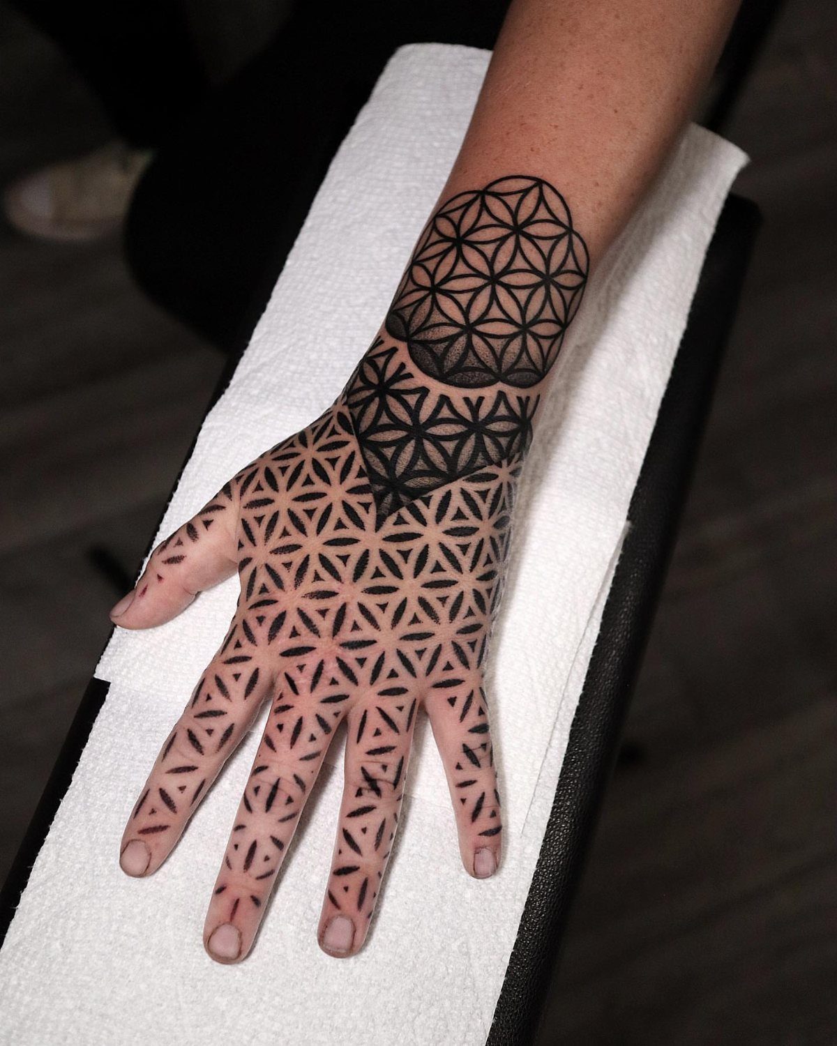 Black ink flower of life and geometric tattoos on a person's hand and wrist.