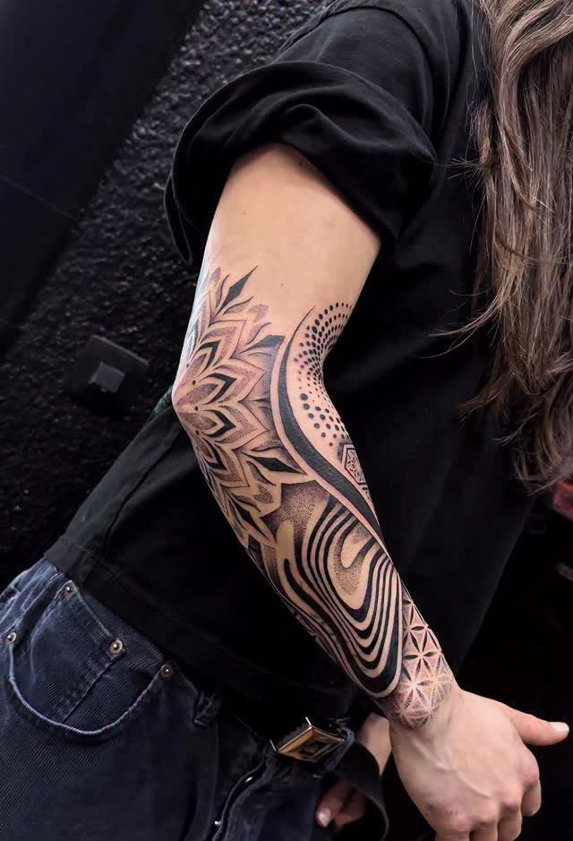 Geometric black ink tattoo on a forearm featuring a mandala and dotwork patterns.