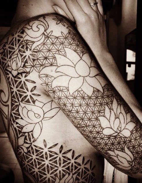 Lotus flowers integrated into a geometric flower of life tattoo on an arm.