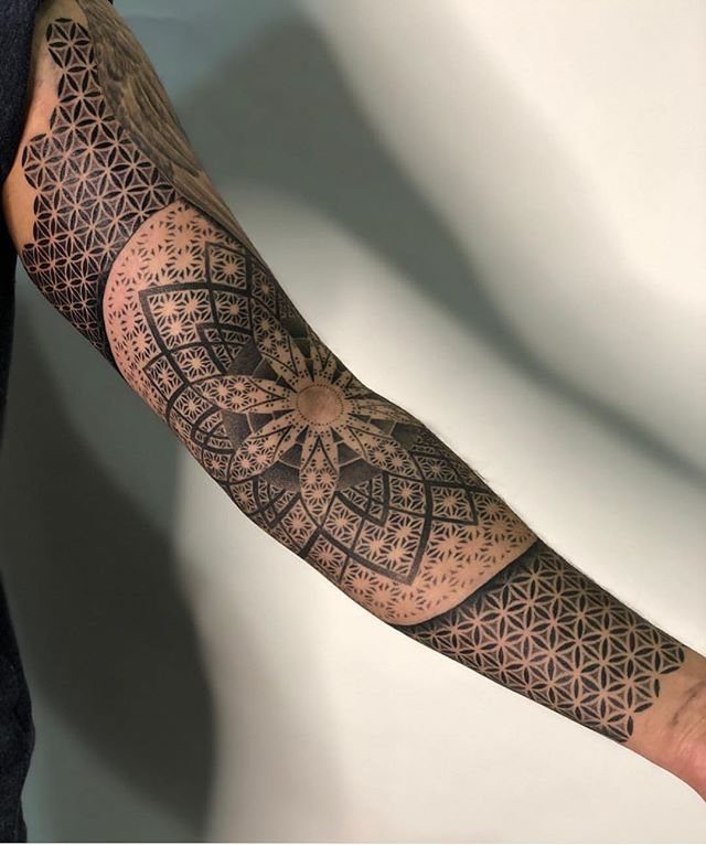 Forearm tattoo featuring a detailed mandala combined with flower of life geometric patterns.