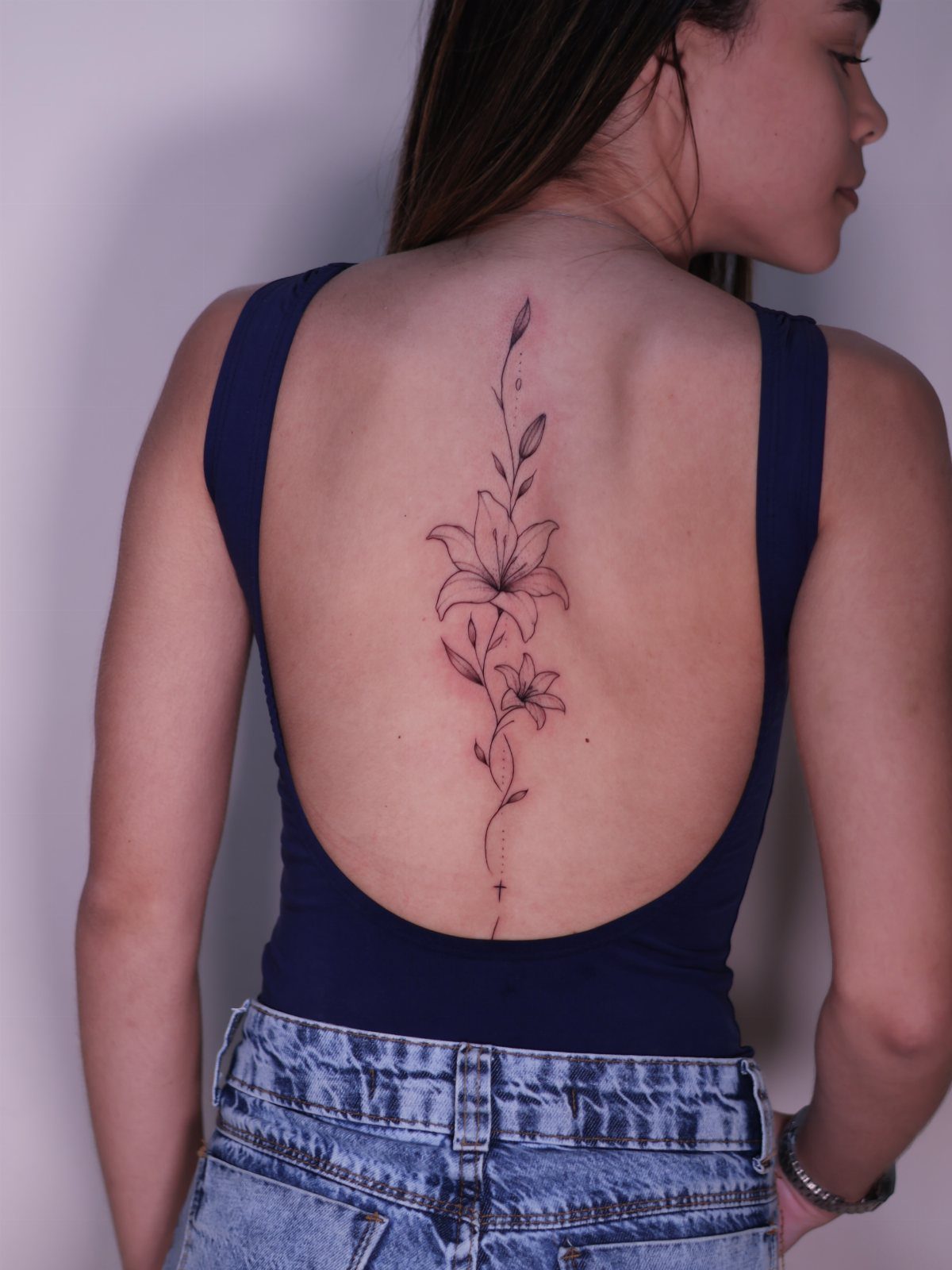 Black ink lily tattoo with leaves running vertically down a woman's spine