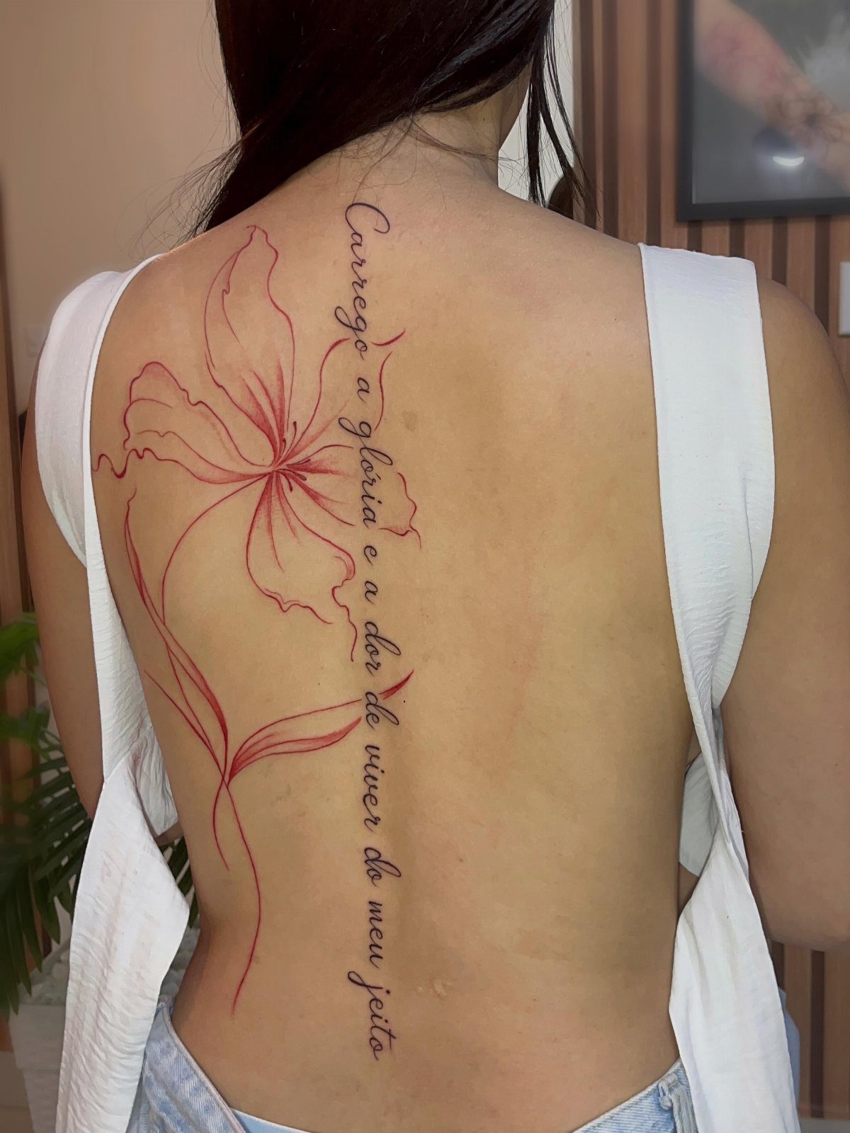 Red ink tattoo of a flower and cursive text along a person's spine