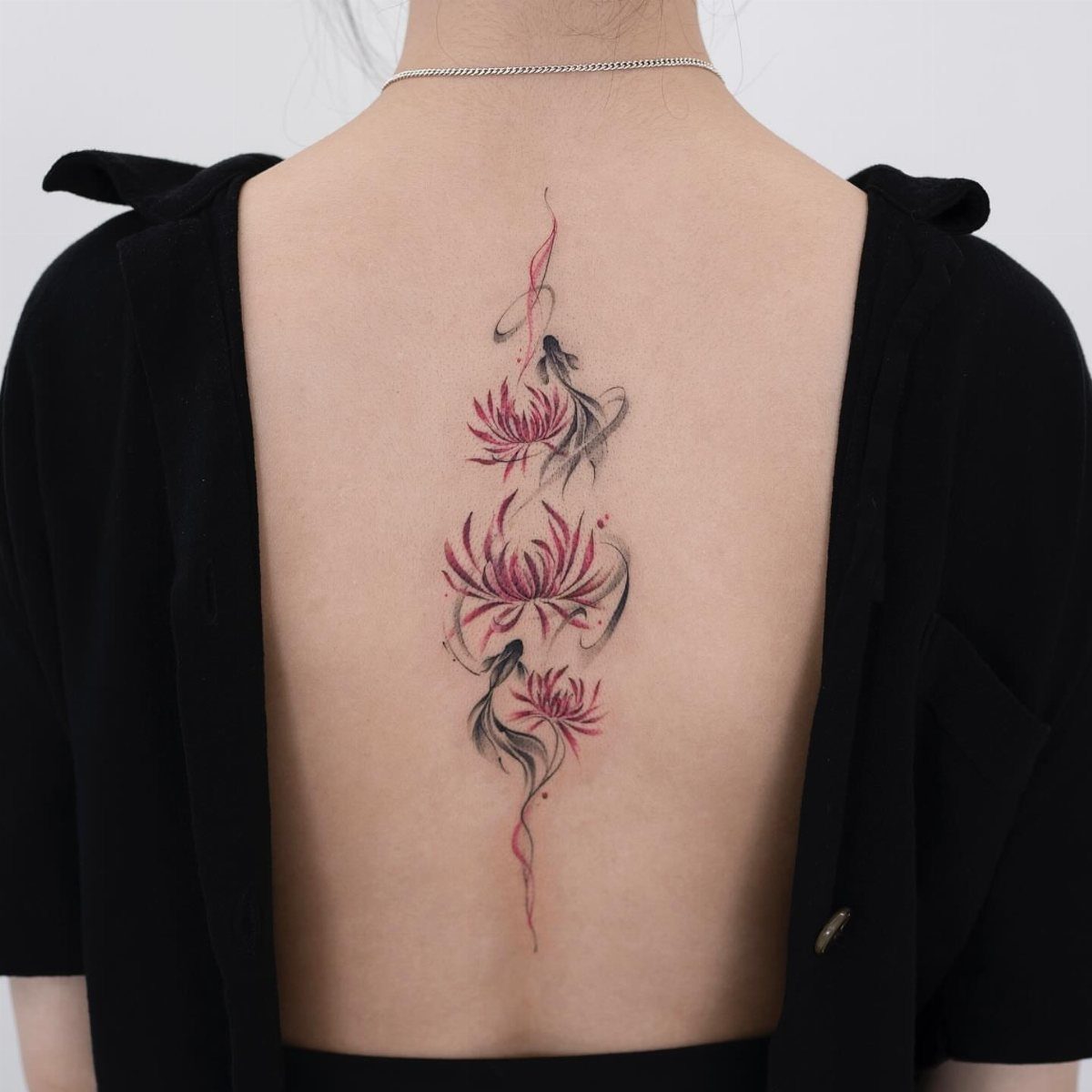 Vertical red and black flower tattoo along the spine of a person's back