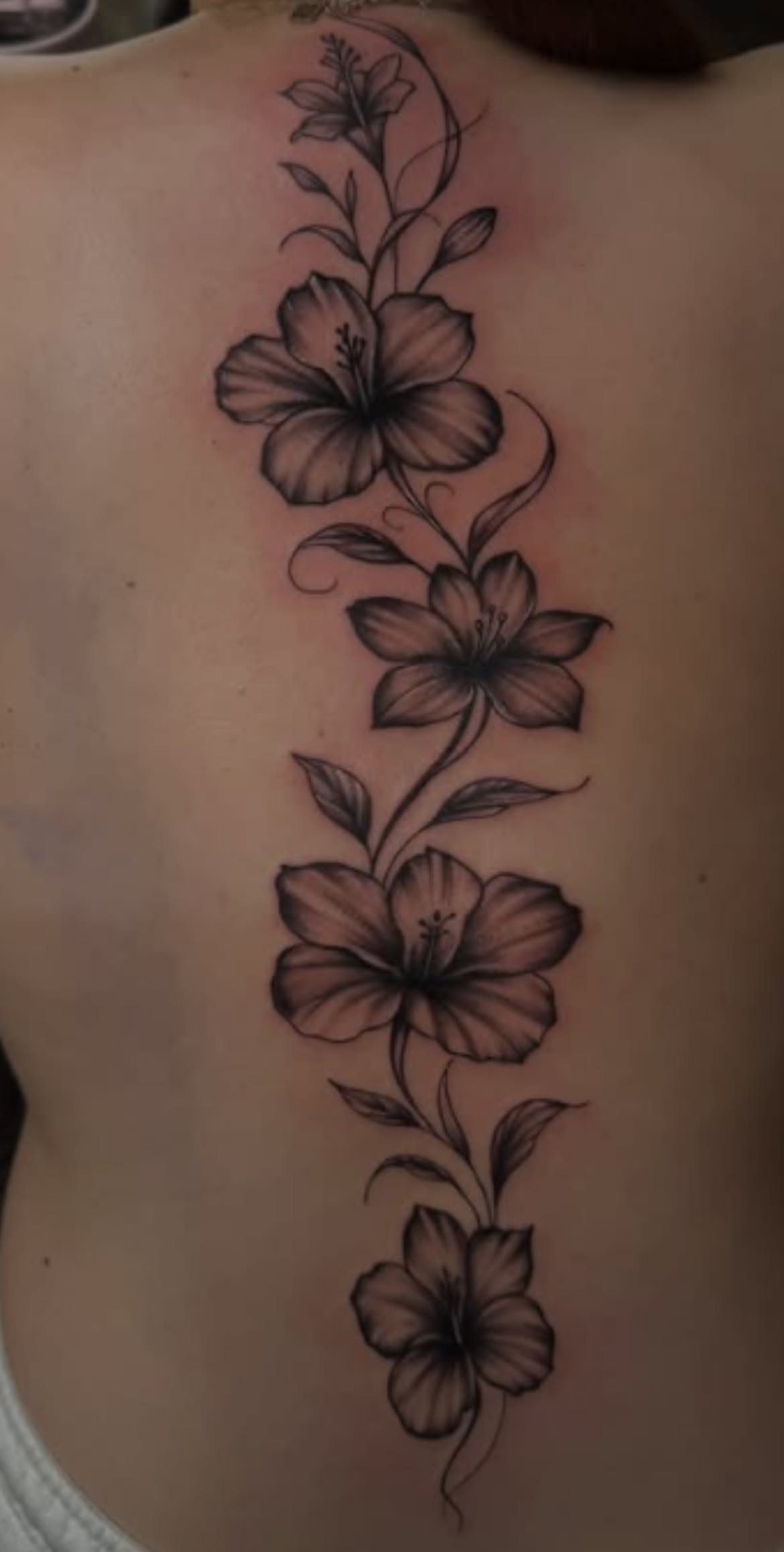 Hibiscus flower tattoo with leaves and vines running down a person's spine.