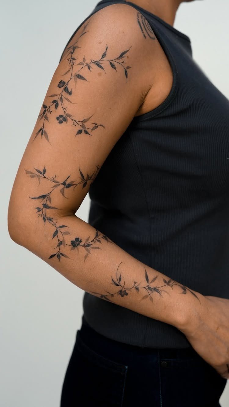 Botanical vine tattoo with leaves and flowers wrapping around a person's arm