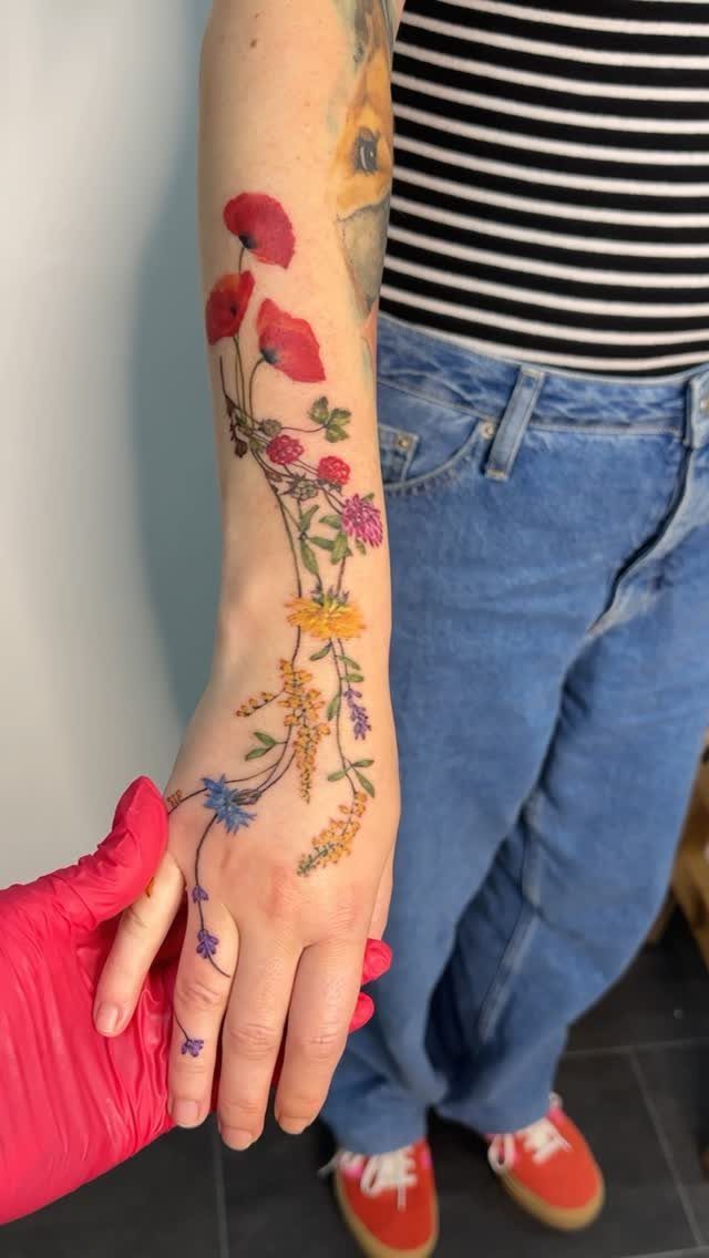 Colorful flower tattoo on a forearm and hand with red, yellow, and purple blooms.