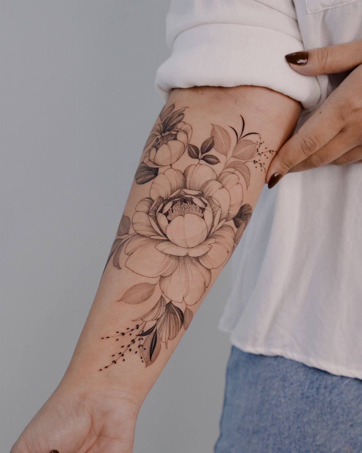 Fine-line flower cluster tattoo on a person's forearm with detailed petals and leaves.