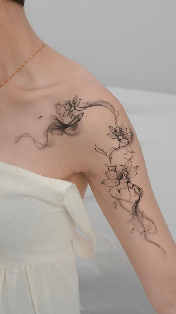 Lotus flower tattoo with flowing decorative lines on a person's shoulder and arm
