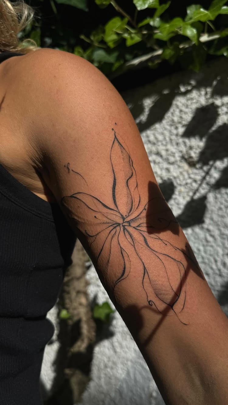 Single line flower tattoo on a person's upper arm against a sunny wall