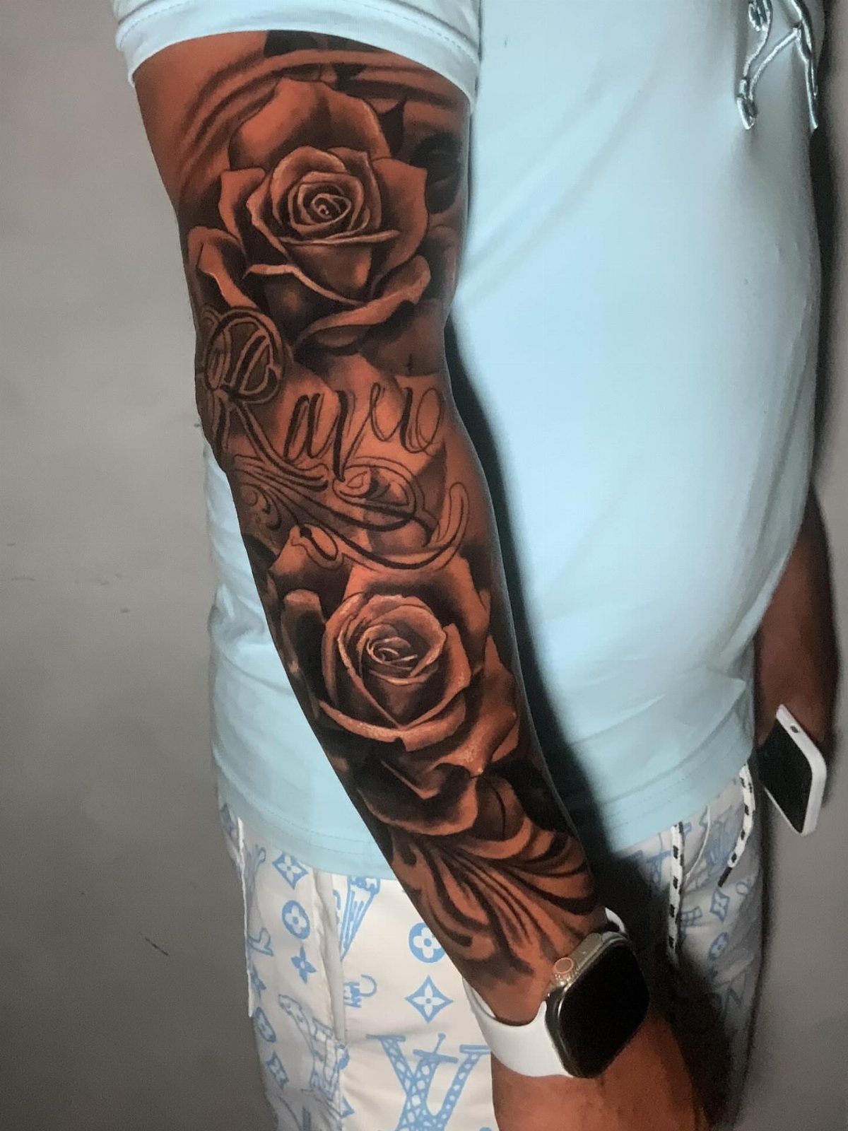 Two shaded roses and script in a vertical tattoo arrangement on a forearm.