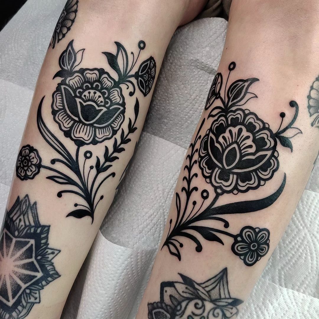 Matching black ink floral tattoos on two forearms with bold stylized flower designs.