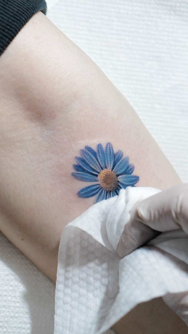 Blue daisy flower tattoo on skin being wiped with a white paper towel
