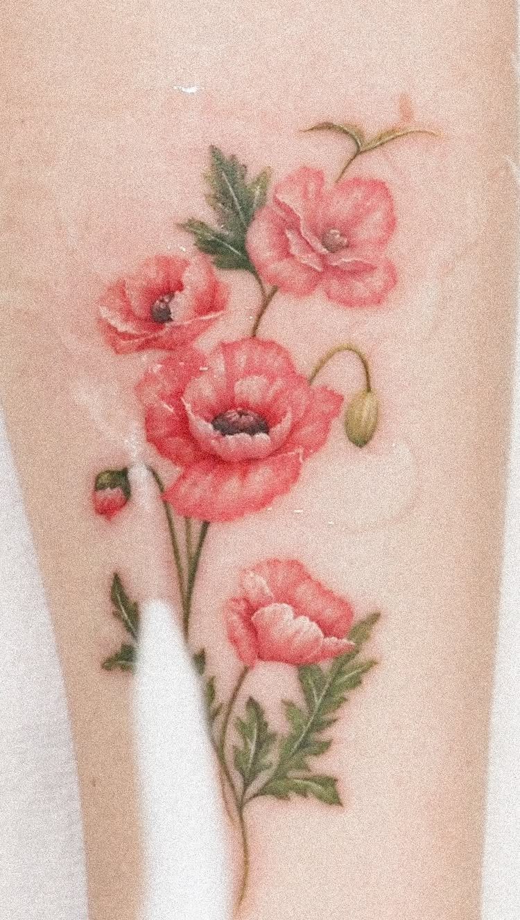 Red poppy flower tattoo with green leaves on a person's arm