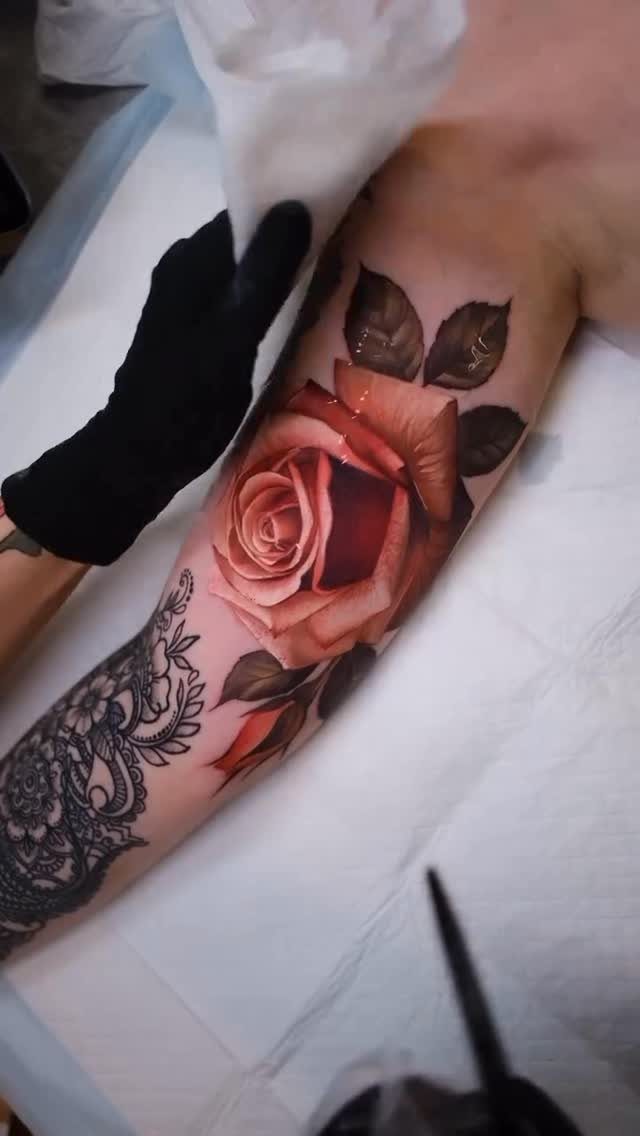 Red rose tattoo on a forearm being wiped with a white paper towel