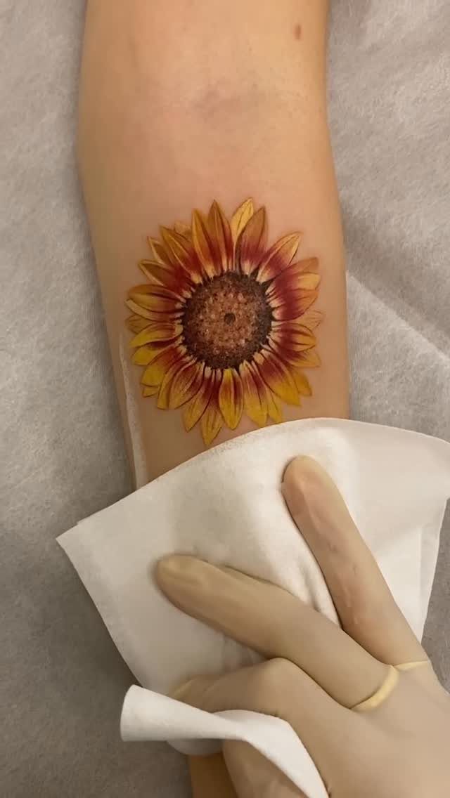 Sunflower tattoo on a forearm being wiped with a white paper towel