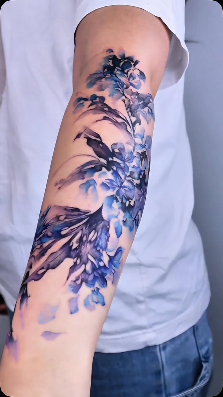 Blue and purple watercolor floral tattoo on a person's forearm