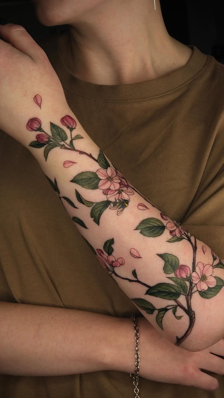 Pink apple blossom tattoo on a forearm with green leaves and branches
