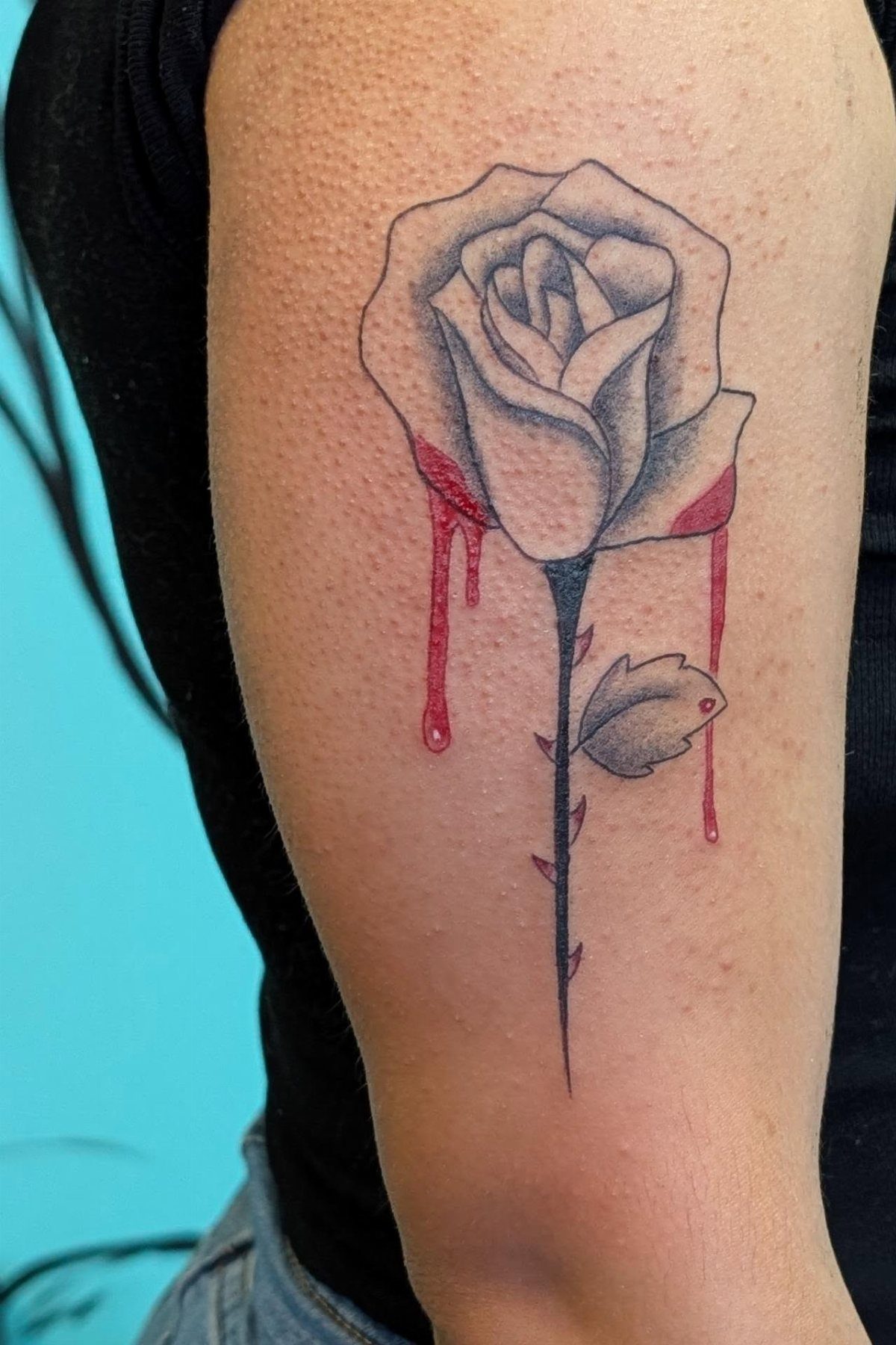 Bleeding rose tattoo on an arm with red drips falling from the petals
