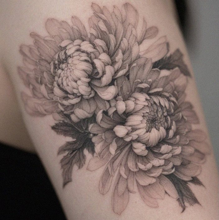 Chrysanthemum flower tattoo with detailed shading and leaves on a person's arm.