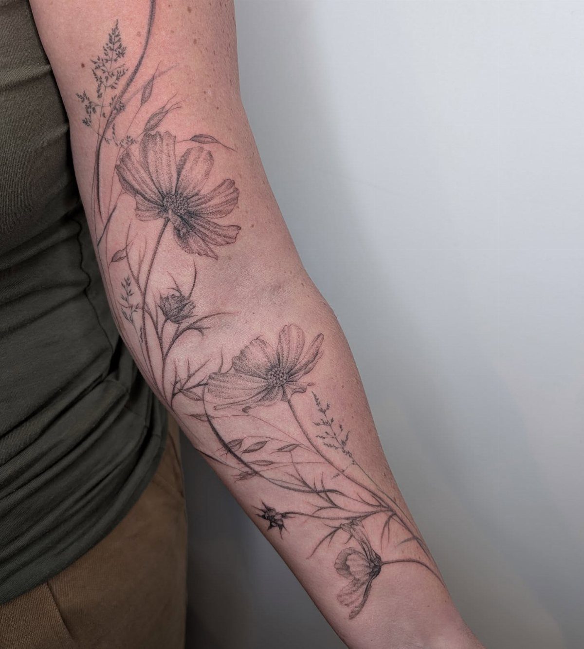 Cosmos flower tattoo with fine black linework on a person's forearm