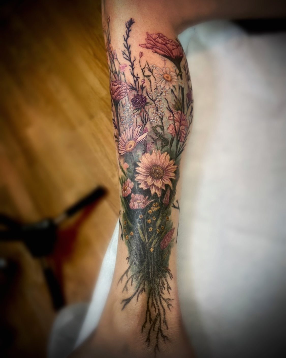 Colorful floral garden tattoo on a forearm featuring various blooms and roots.