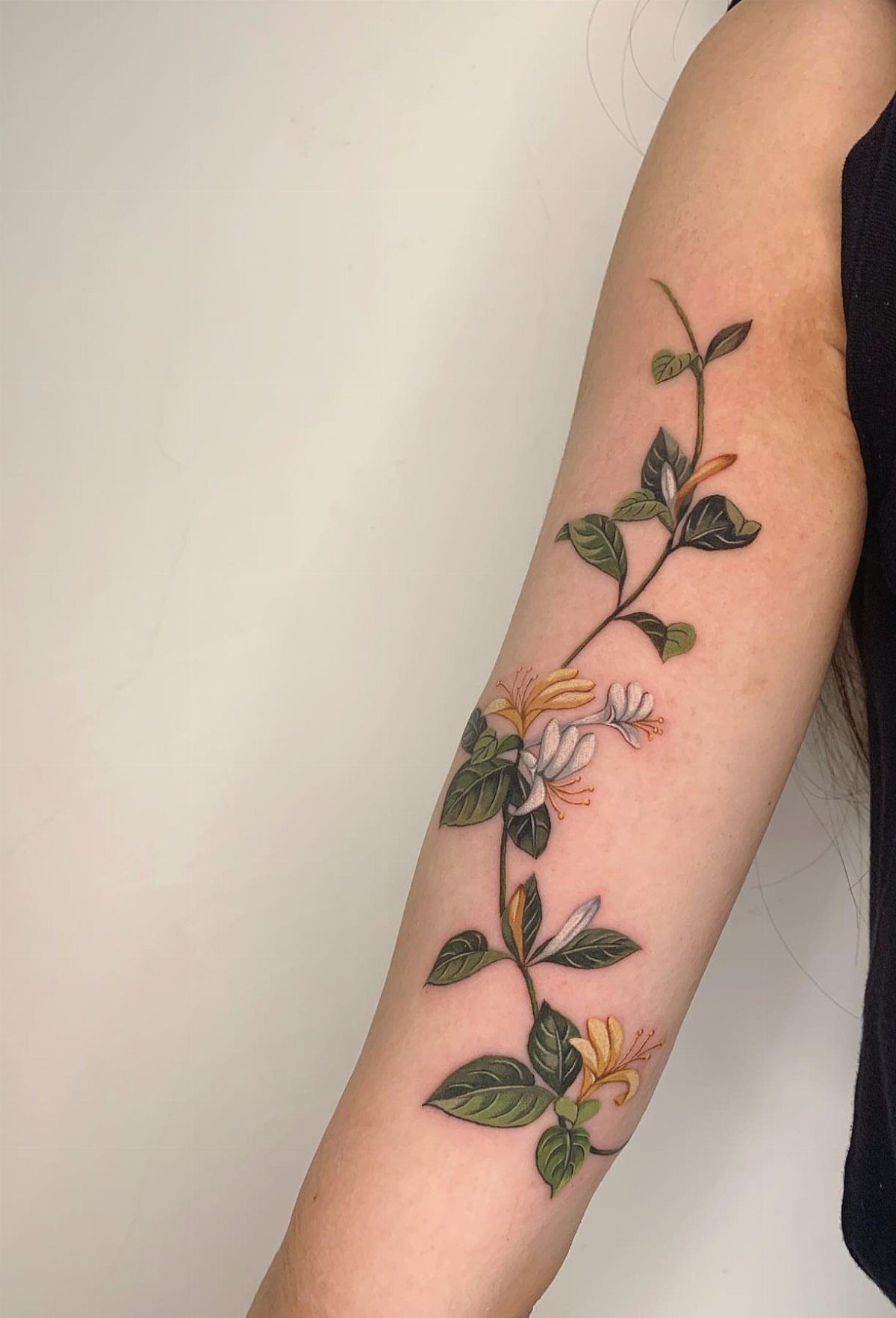 Floral vine tattoo with white and yellow blossoms on a person's forearm