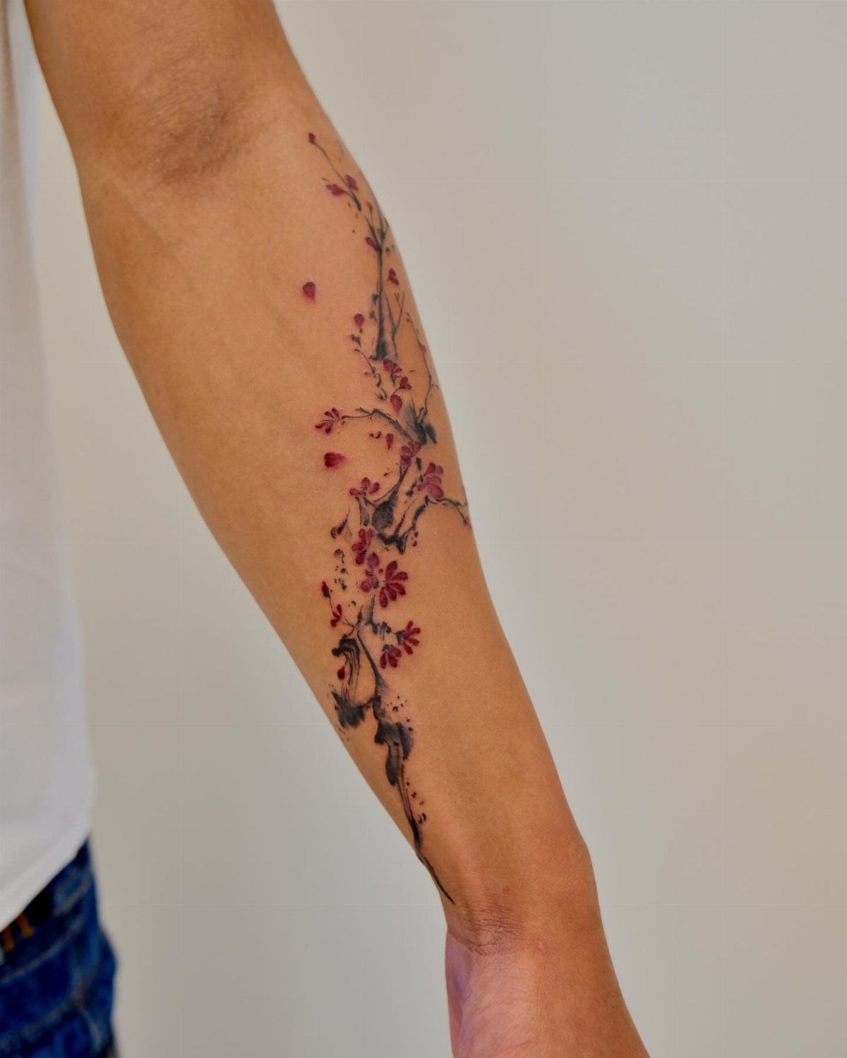 Tattoo of a winding branch with red plum blossoms on a person's forearm