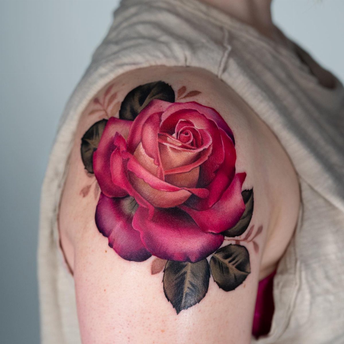 Red rose tattoo with green leaves on a person's shoulder
