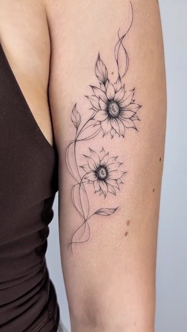 Two sunflower tattoos with delicate stems and leaves on a person's upper arm