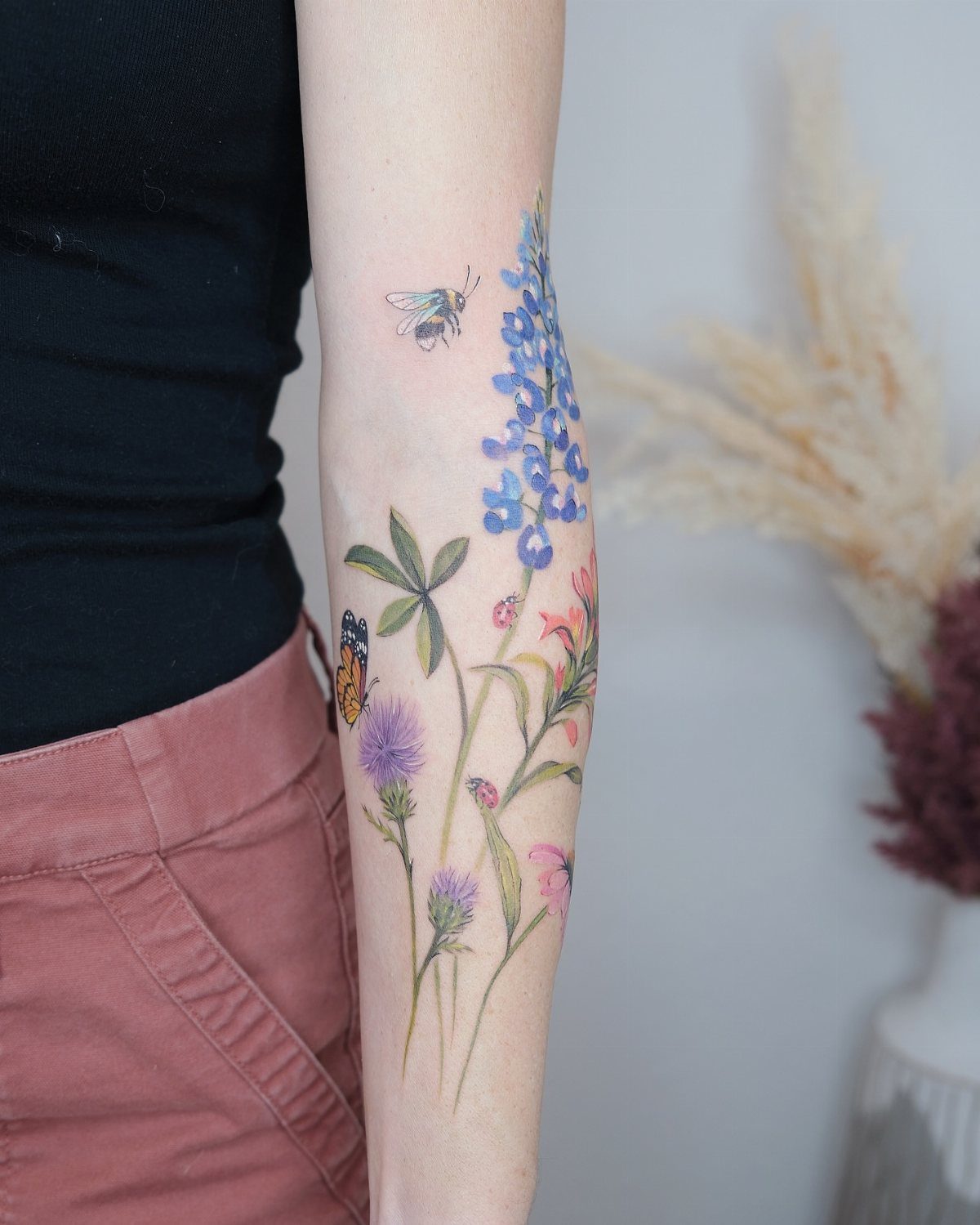 Colorful wildflower bouquet tattoo on a forearm with a bee and butterfly