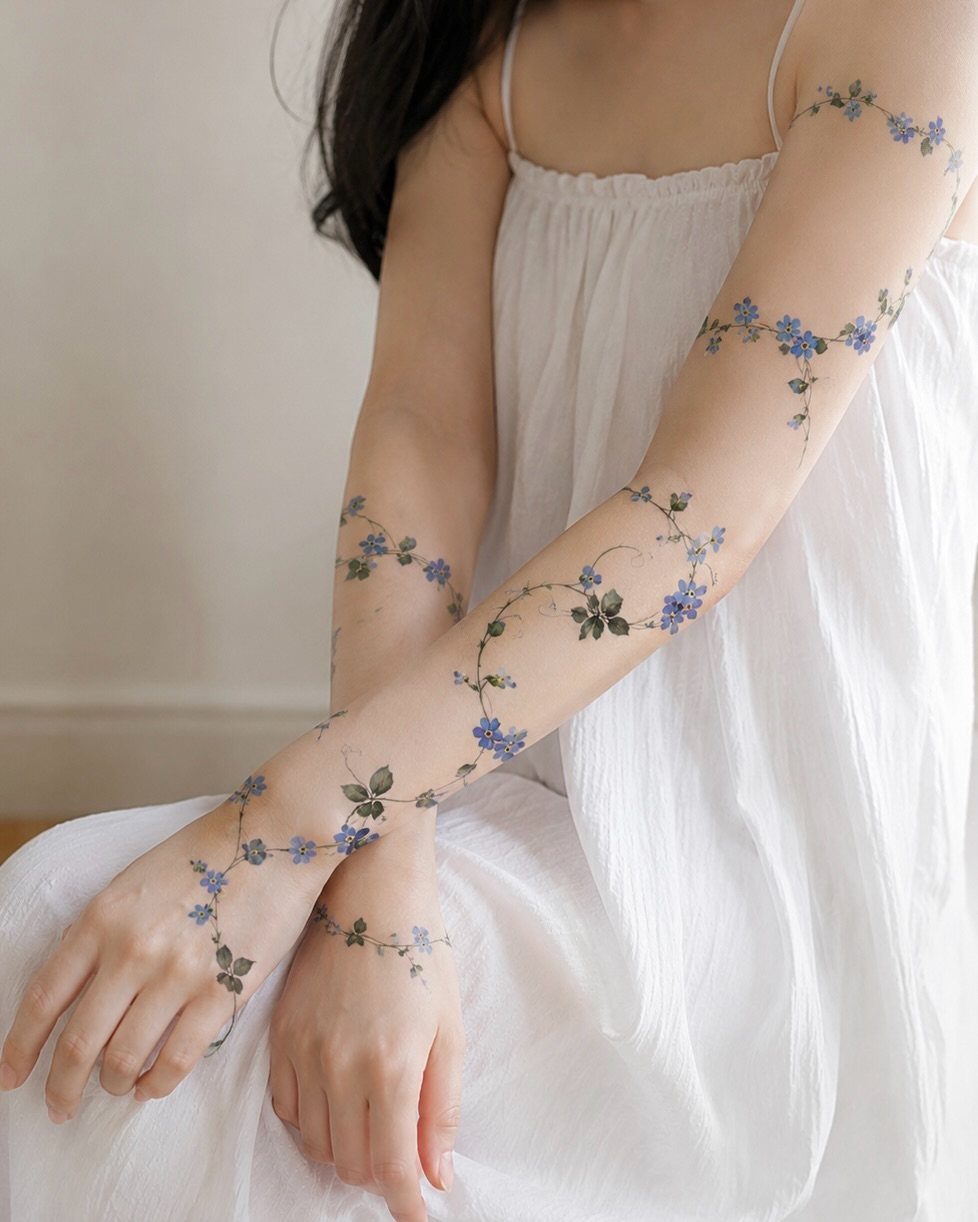 Blue flower tattoos winding around the arms and wrists of a person.