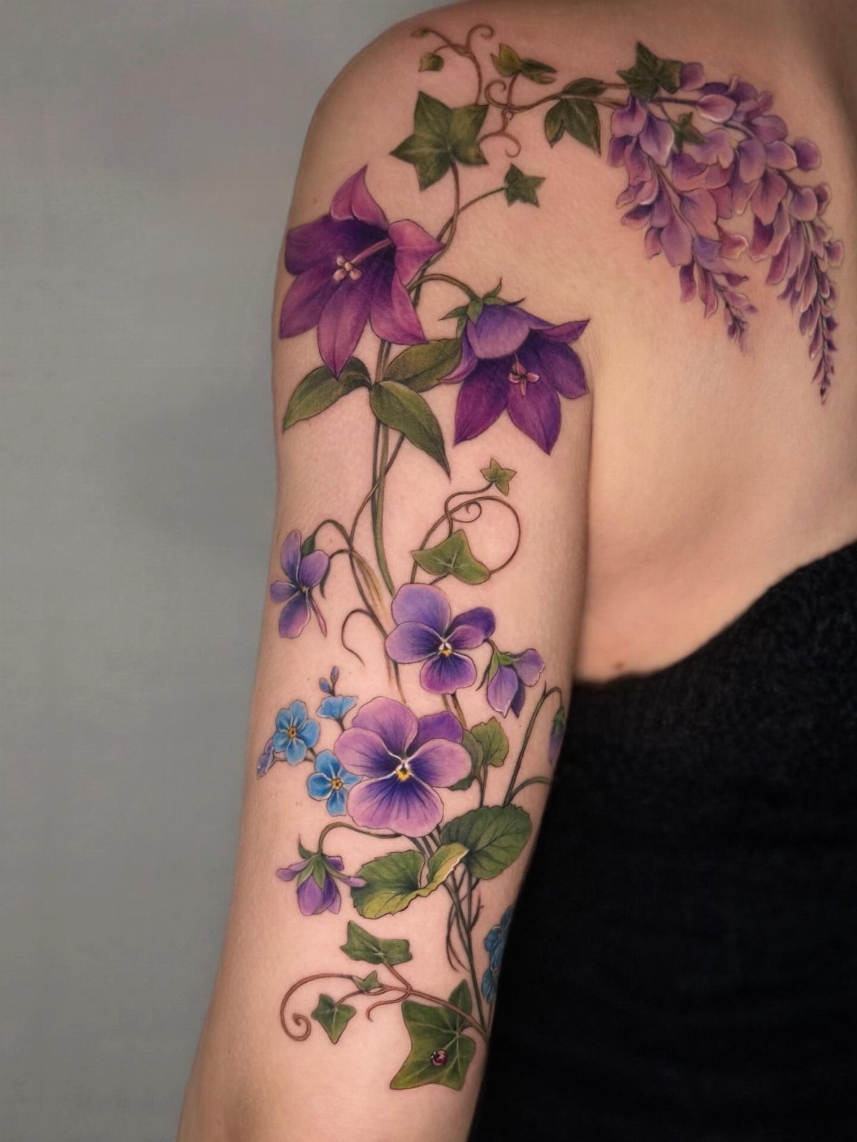 Purple wisteria and mixed floral tattoo winding down a person's shoulder and arm.