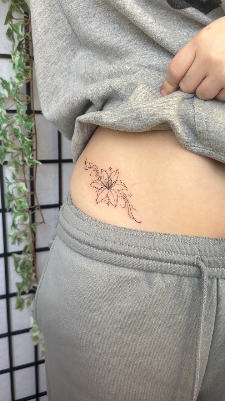Lily flower line tattoo on a person's hip with grey clothing background