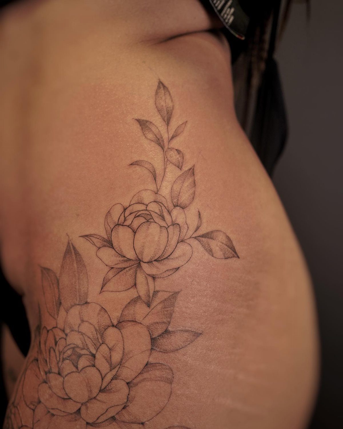 Floral tattoo on a hip featuring two large blooming flowers and delicate leaves.