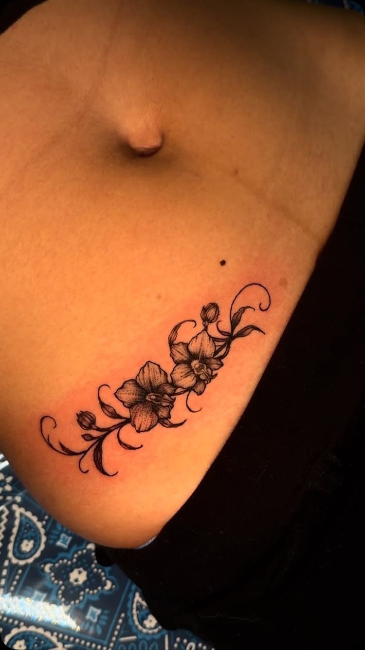 Orchid flower tattoo with elegant swirls on a person's hip and lower abdomen.