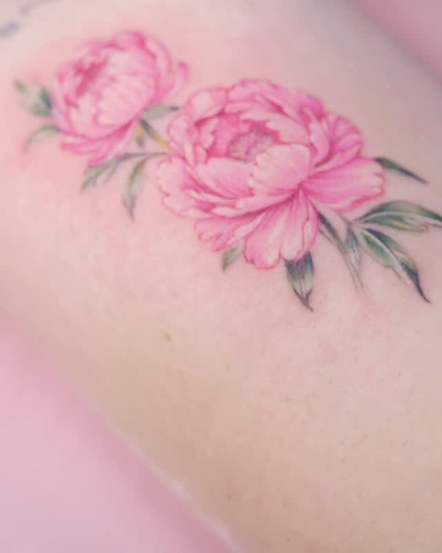 Pink peony flower tattoos with green leaves on a person's hip.