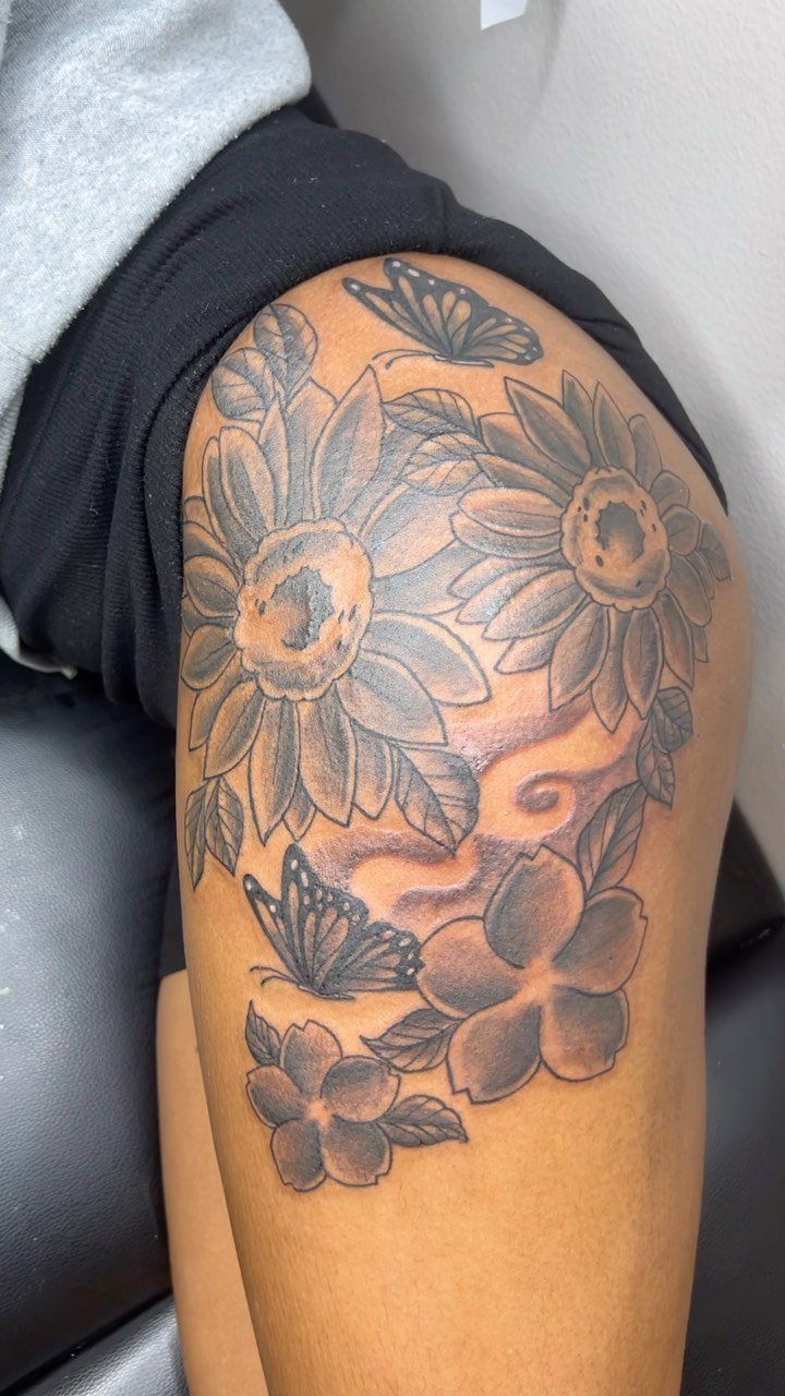 Sunflowers and butterflies tattoo in black and grey ink on a person's hip.