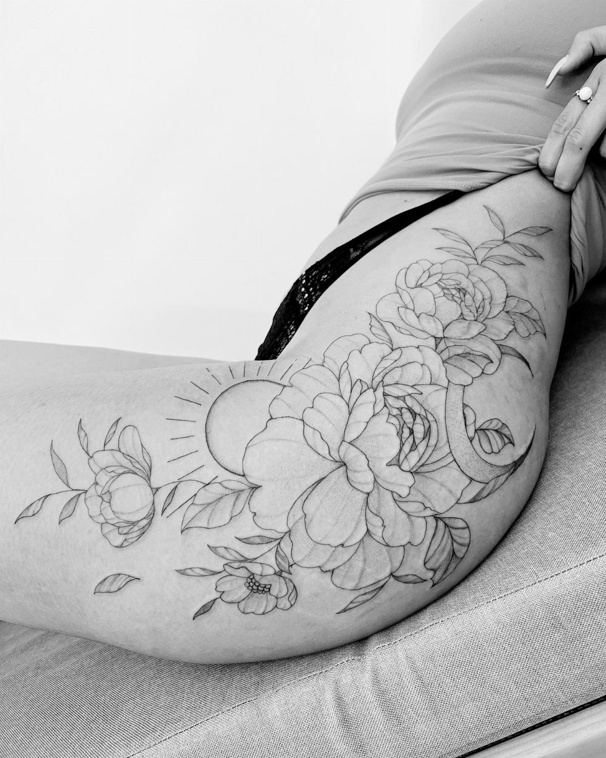 Floral tattoo outline on a thigh featuring peonies, a sun, and a crescent moon.