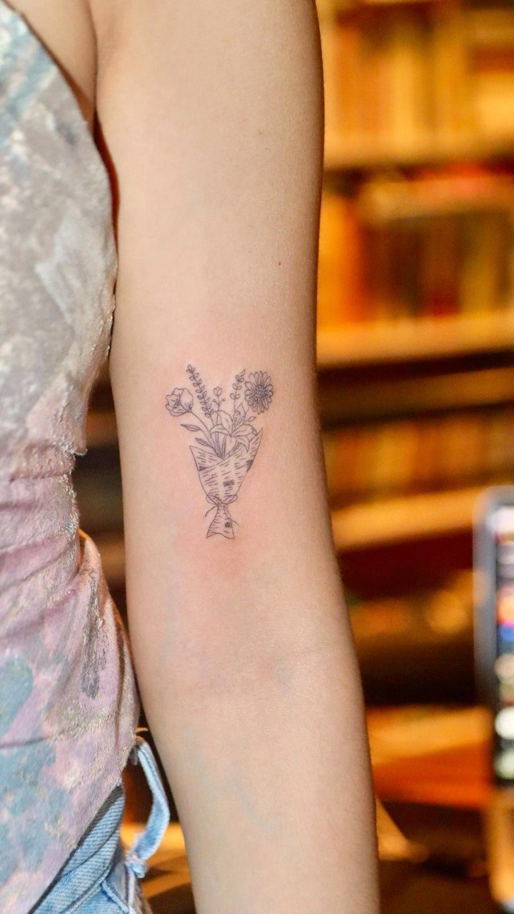 Minimalist flower bouquet tattoo outline on a person's inner forearm