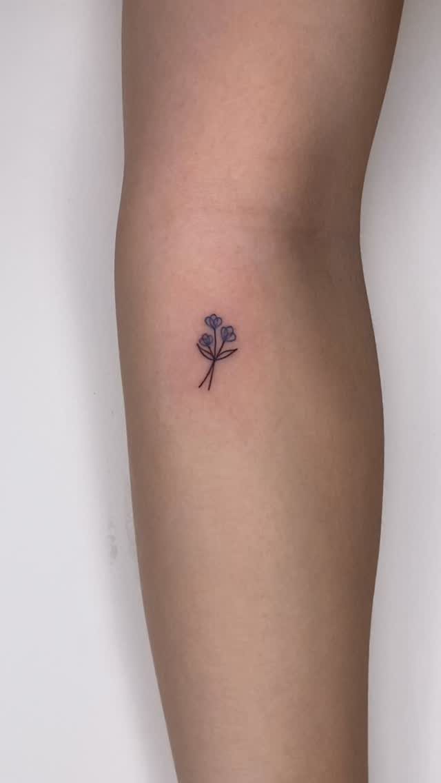 Small blue flower tattoo with a thin stem on a person's leg