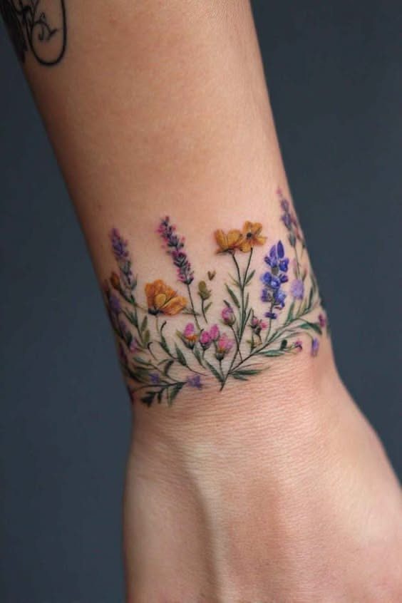 Colorful wildflower tattoo wrapped around a wrist like a floral bracelet band