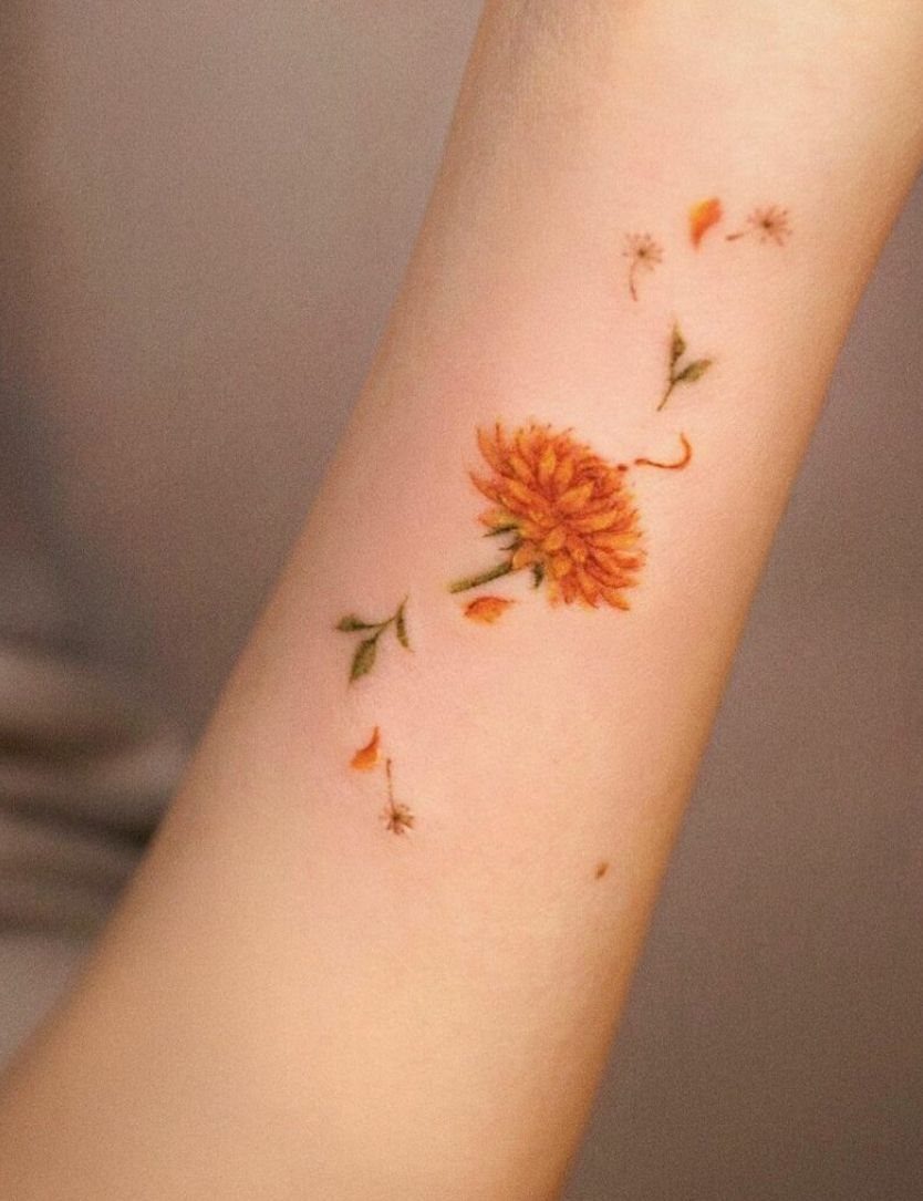 Orange flower tattoo on a wrist with floating petals and green leaves