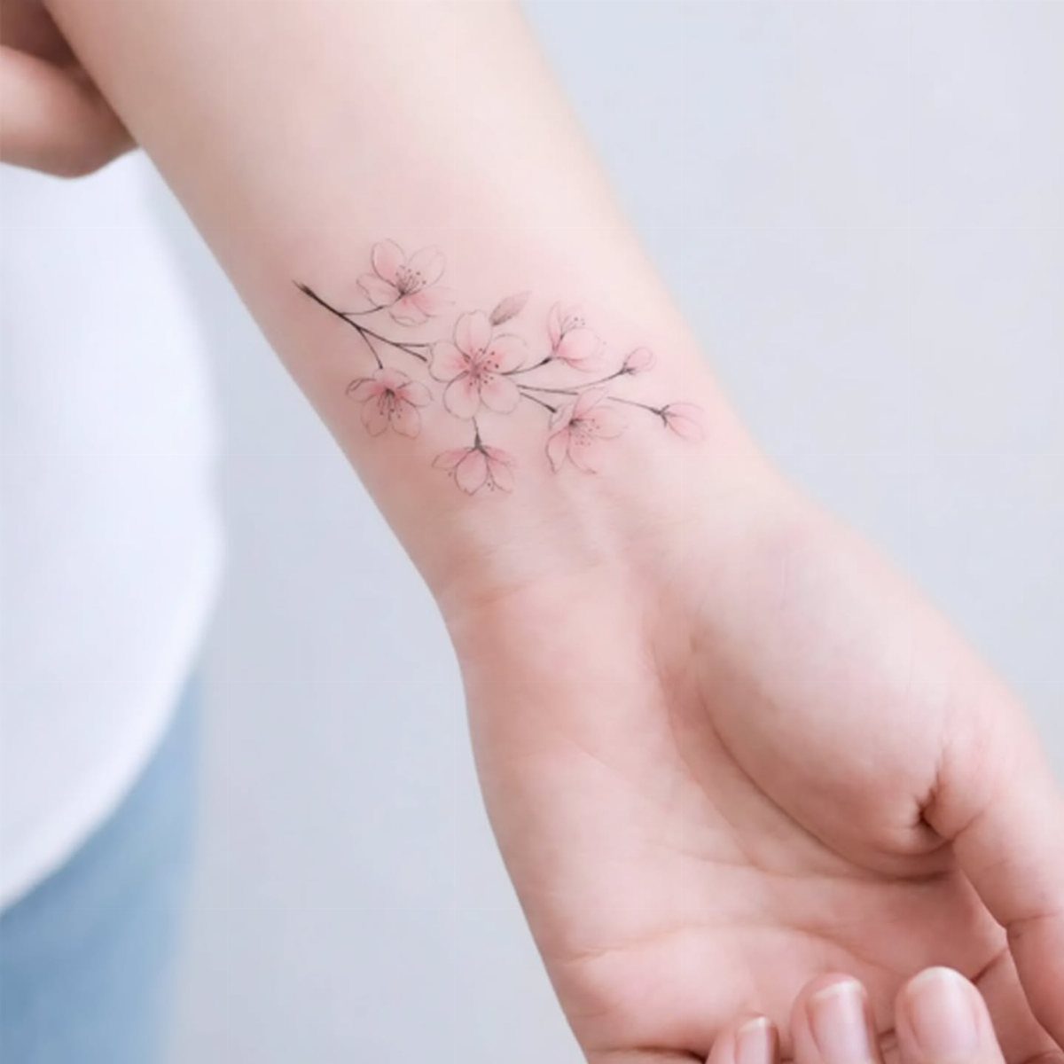Cherry blossom tattoo with pink flowers on a person's inner wrist