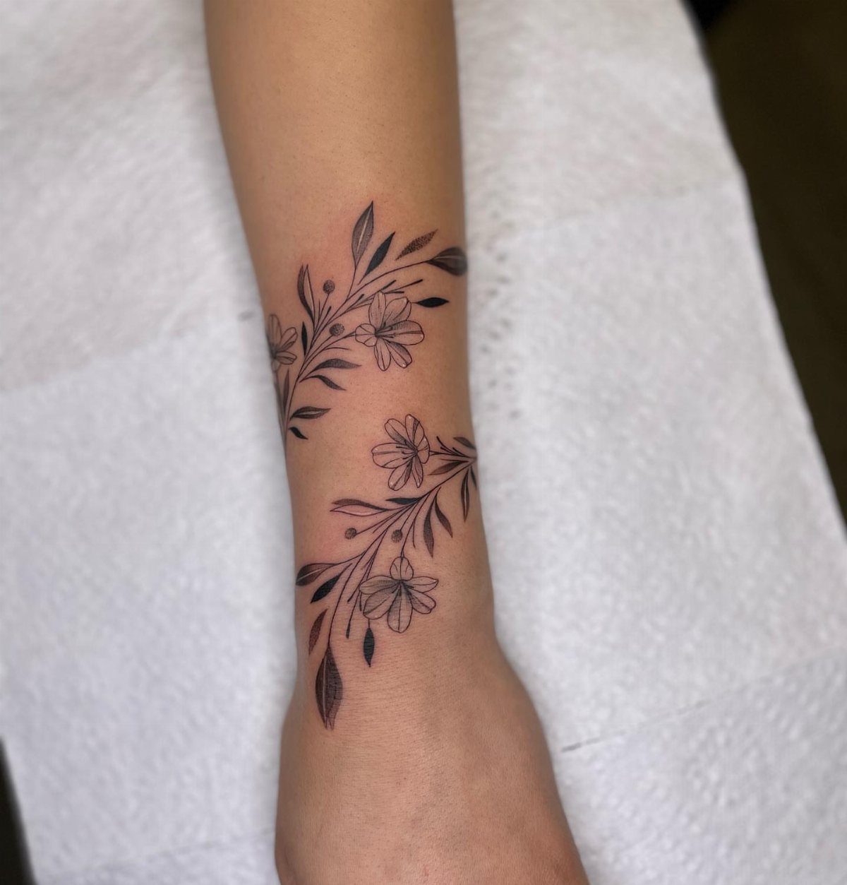Floral vine tattoo with small black flowers wrapping around a person's wrist