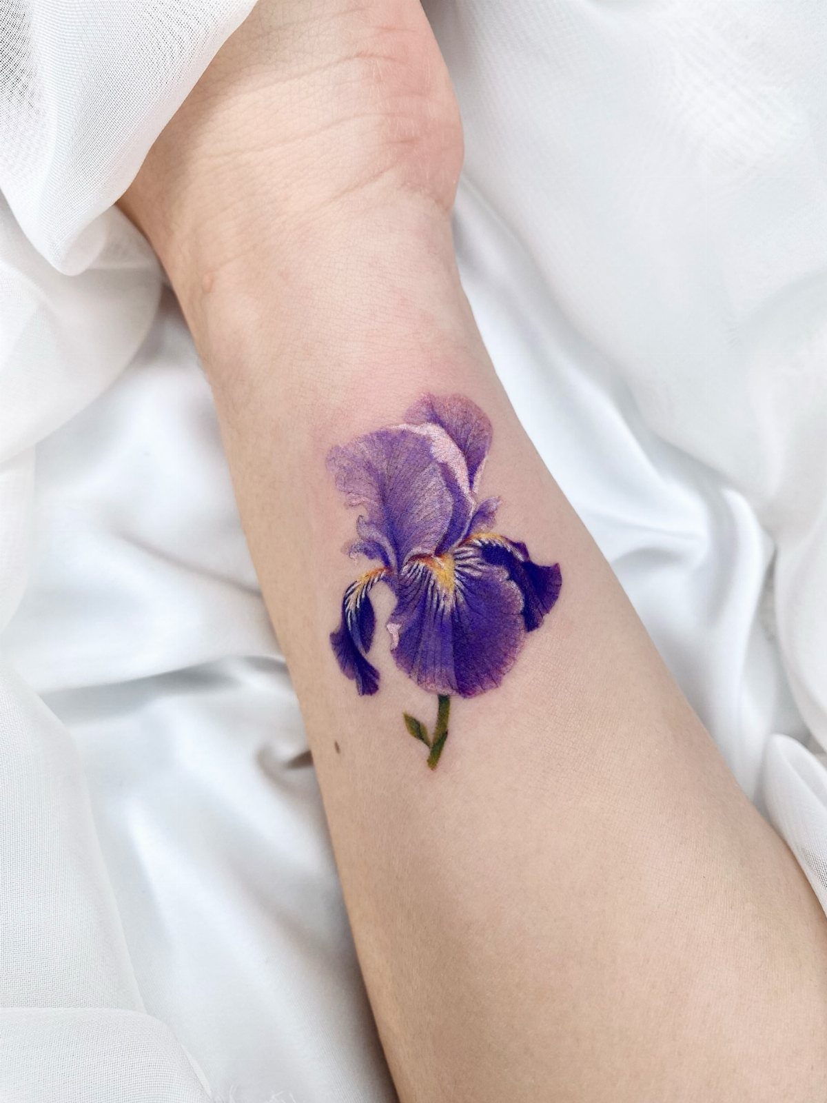 Purple iris flower tattoo on a person's inner wrist against white fabric