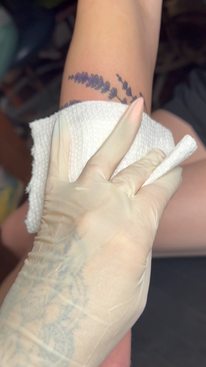 Purple lavender flower tattoo on a wrist being wiped with a paper towel