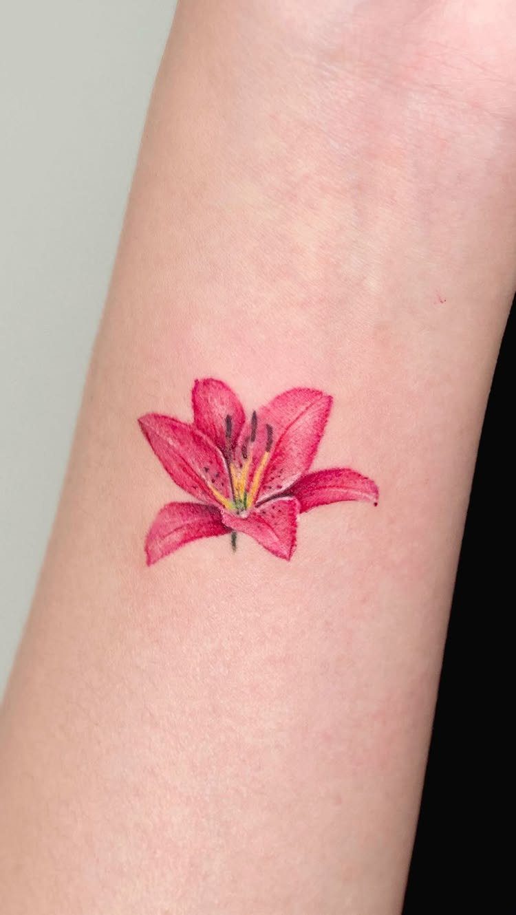 Red lily flower tattoo on a person's inner wrist with yellow center details.