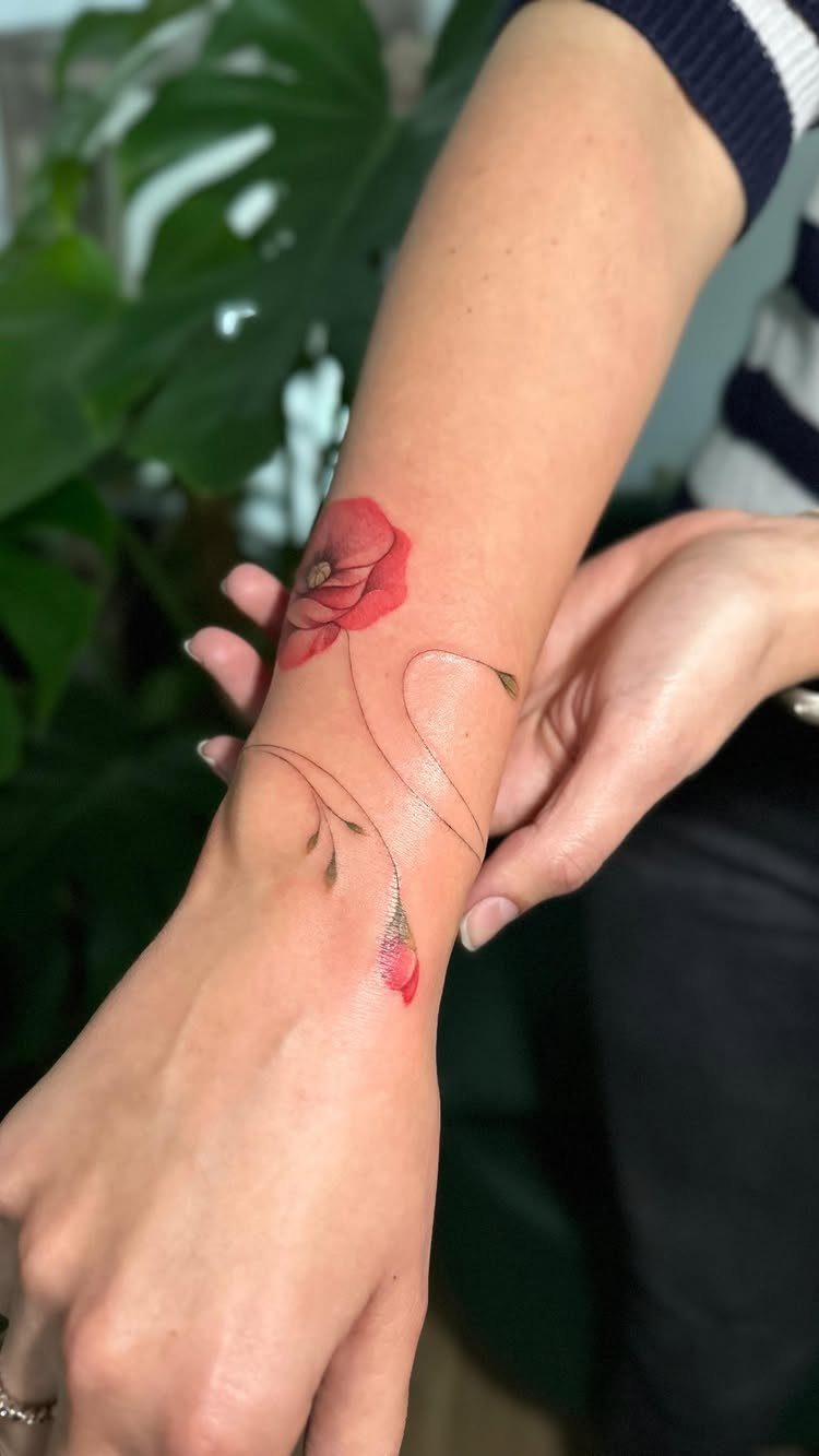Red poppy flower tattoo on a wrist with delicate curving stems and buds